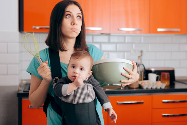 busy mom cooking  holding baby in carrier babywearing system - mother emotional stress exhaustion cooking imagens e fotografias de stock