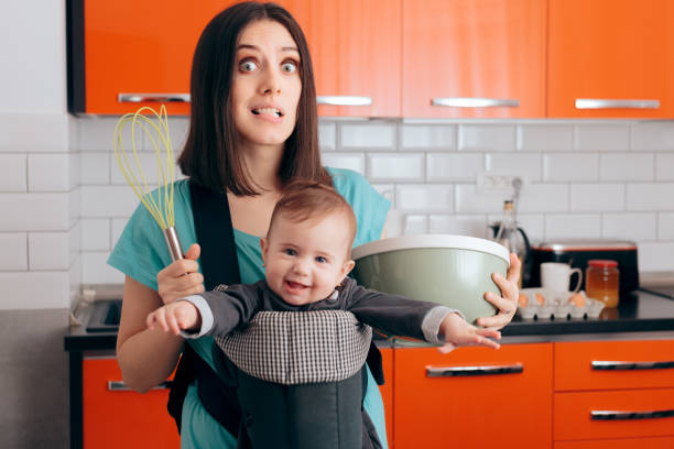 mamma impegnata che cucina tenendo il bambino nel sistema di babywearing carrier - mother emotional stress exhaustion cooking foto e immagini stock