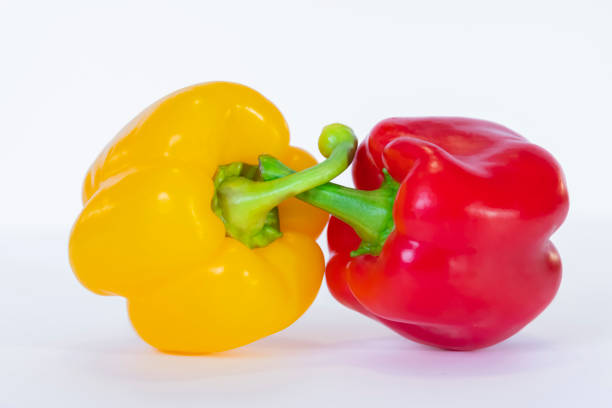 Close-up of a couple of yellow and red bell peppers crossing their pedicels on a light background. Healthy food concept.