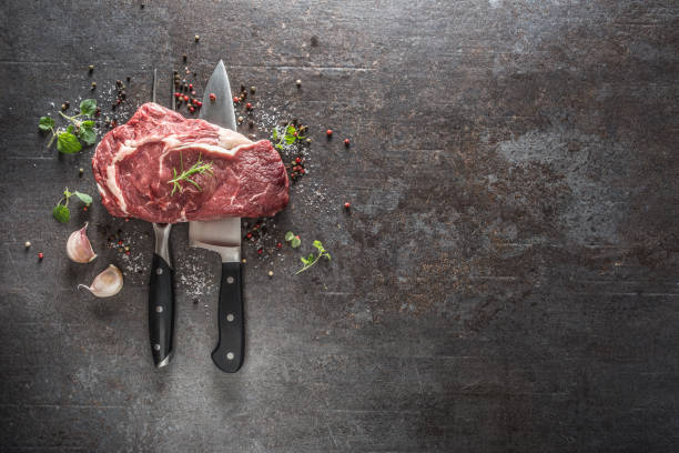 istock Raw beef steak with fork and knife salt pepper and herbs on dark concrete background 1200862081