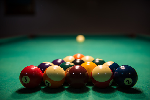 Male lines up billiard shot to sink a ball by the corner pocket