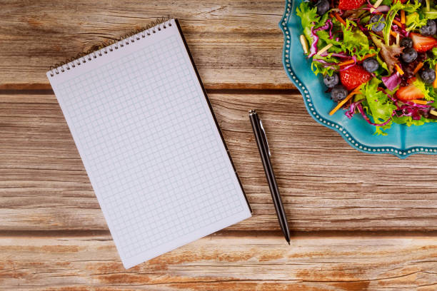 istock Notepad and pen with salad on wooden background. 1200864060