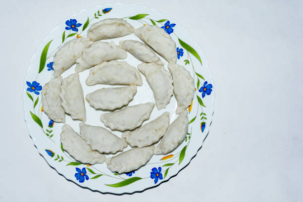 Bengali cuisine - puli pitha in a ceramic plate on white background. It is a traditional bengali dumplings recipe where the dumplings are made with rice flour and filled with kheer or coconut.