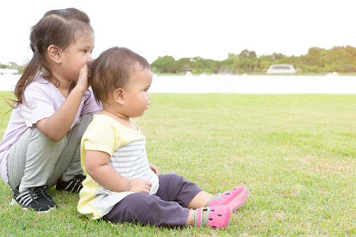 Two baby girls sitting and showing care and love to younger sister. Sisters sitting and enjoy in the park.