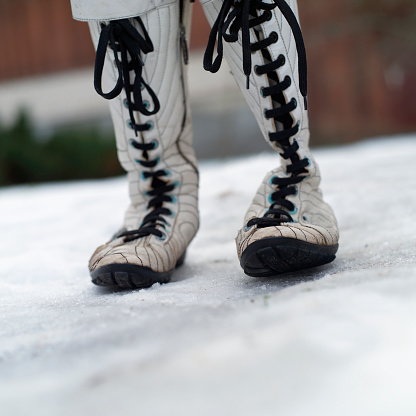 Woman wearing white leather boots walking on the snow, shallow DOF