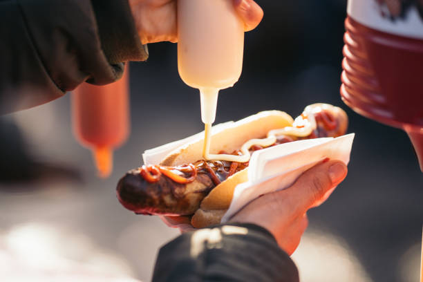 kobieta wylewa sos pomidorowy, majonez i musztarda na grillowanej kiełbasie wieprzowej bratwurst na niemieckim rynku. - hot dog snack food ketchup zdjęcia i obrazy z banku zdjęć