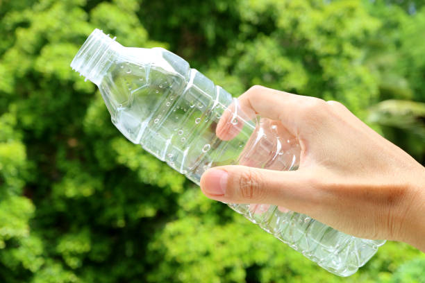 segurando uma garrafa de plástico vazia de água potável com folhagens verdes embaçadas no pano de fundo - water bottle sports and fitness selective focus sport - fotografias e filmes do acervo