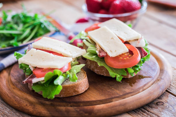 Simple, rich breakfast on table, sandwiches with pancetta, havarti cheese slices, lettuce and arugula, close-up, no people