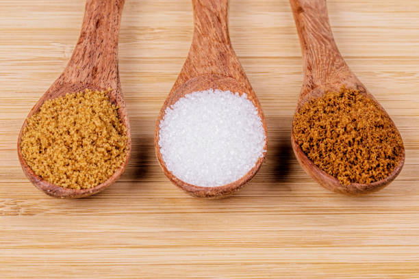 Three wooden spoon full of different sugars, light brown sugar, dark brown sugar, and granulated sugar on a wooden background