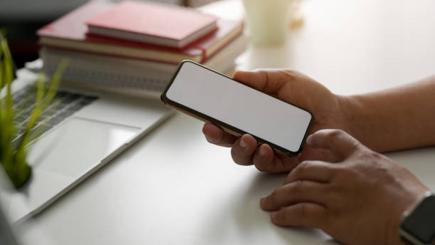 istock Side view of businessman using blank screen smartphone in modern workspace with laptop and office supplies 1200894655