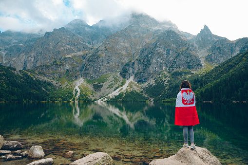young woman covered with poland flag looking at lake in tatra mountains in carpathian
