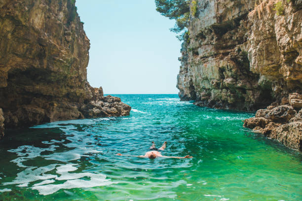 young man swimming on back in sea at bay between cliffs summer time copy space