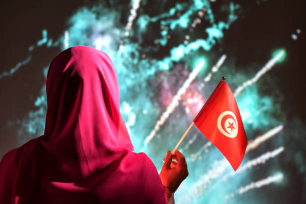 mulher muçulmana em um cachecol segurando bandeira da tunísia durante fogos de artifício à noite. - eastern european flash - fotografias e filmes do acervo