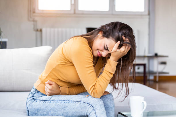 junge kranke frau mit händen halten drücken ihren schritt unterbauch. medizinische oder gynäkologische probleme, gesundheitskonzept. junge frau leidet unter bauchschmerzen beim sitzen auf dem sofa zu hause - eileiterschwangerschaft stock-fotos und bilder