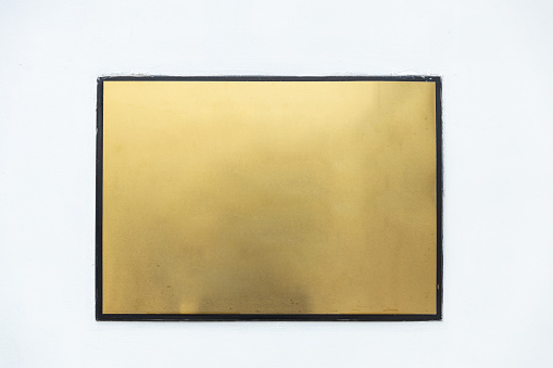 empty metallic golden plate sign with black border on white cement wall