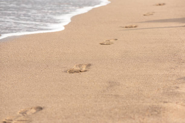 istock Footprints in the sand and wave with foam. 1200900925