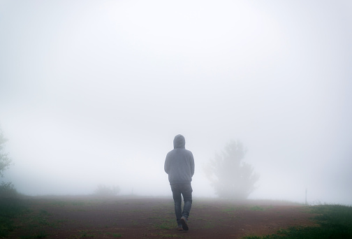 Man walking alone on dark misty foggy misty road.