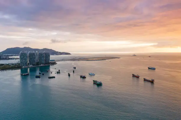 Aerial view of buildings and ships in the sea of Sanya, China covered by colorful clouds during sunset