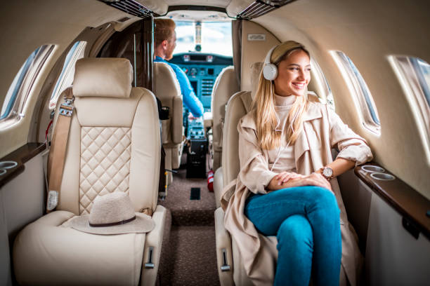 joven, mujer rubia de moda disfrutando de la música sobre los auriculares mientras vuela a bordo de un jet privado - status symbol audio fotografías e imágenes de stock