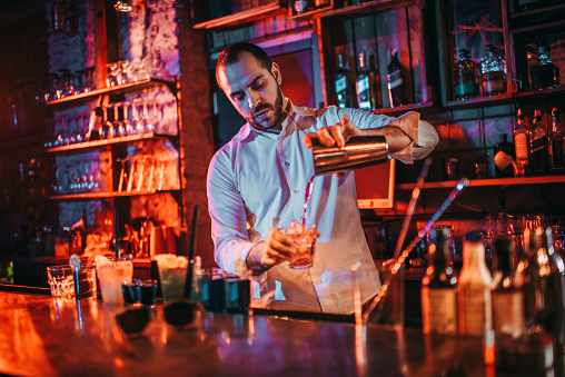 Barkeeper pouring shots from a shaker at a bar.