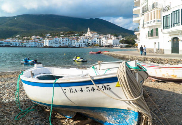 Cadaqués, Catalonia / Spain - November 30th, 2019: Mediterranean fishing boat on the shore with the old village in the distance