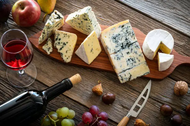 Blue cheese and red wine in cutting board with knife on wooden table