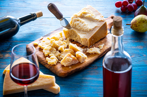 Parmesan Reggiano cheese with red wine and fruits on cutting board and knife at blue wood table
