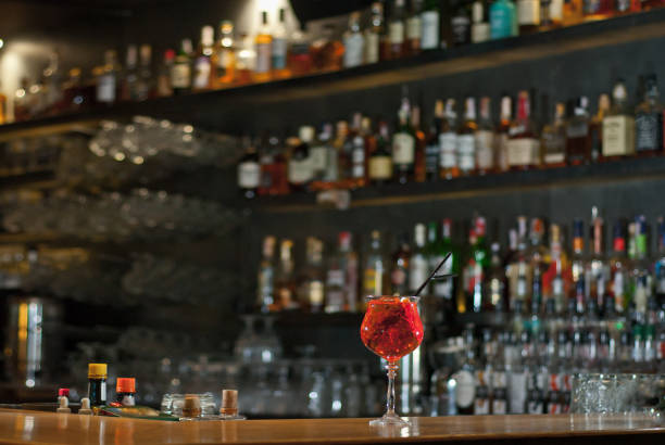 istock Red cocktail on bar counter. Drink with martini, gin, rum, tequila and fruit on the background of bottles with alcohol. Glass with booze on a wooden board. 1200917585