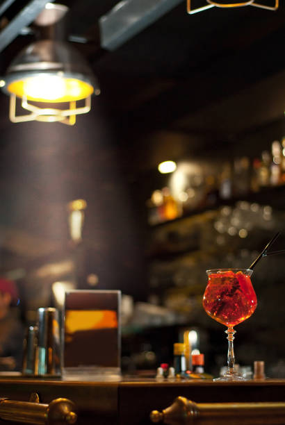 istock Red cocktail on bar counter. Drink with martini, gin, rum, tequila and fruit on the background of bottles with alcohol. Glass with booze on a wooden board. 1200917607