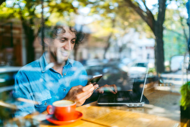 Young handsome Caucasian man using laptop and smartphone at a cafe.