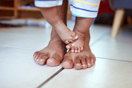 Cropped shot of an unrecognizable father’s feet and his baby’s feet at home