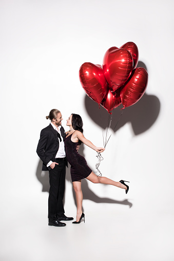 smiling couple holding red heart shaped balloons on valentines day on white