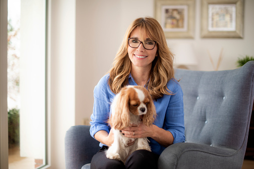 Portrait shot of middle aged woman with toothy smile sitting in armchair with her cute puppy.