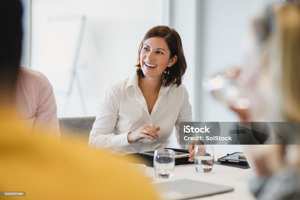 Cheerful mid adult woman smiling at business meeting Businesswoman smiling at meeting table, listening, learning, success, happiness Business Stock Photo