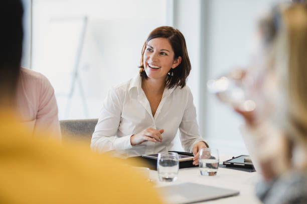 Cheerful mid adult woman smiling at business meeting Businesswoman smiling at meeting table, listening, learning, success, happiness commercial activity photos stock pictures, royalty-free photos & images