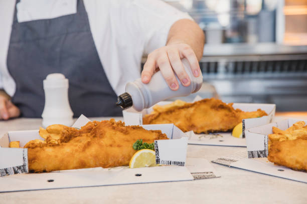 istock Close up of boxes of fish and chips having vinegar added 1200928721