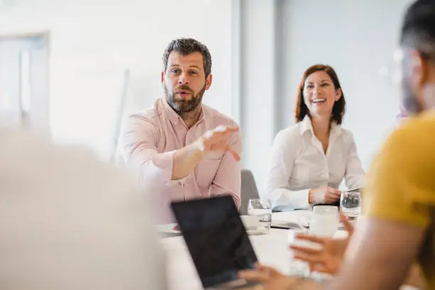 Mature man in his 40s gesturing and talking, sitting at meeting table in board room, discussion, collaboration, strategy