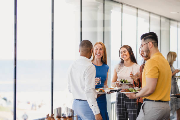 Group of cheerful colleagues enjoying lunch break at event Happy coworkers discussing with buffet food, networking, friendship, corporate business lunch stock pictures, royalty-free photos & images