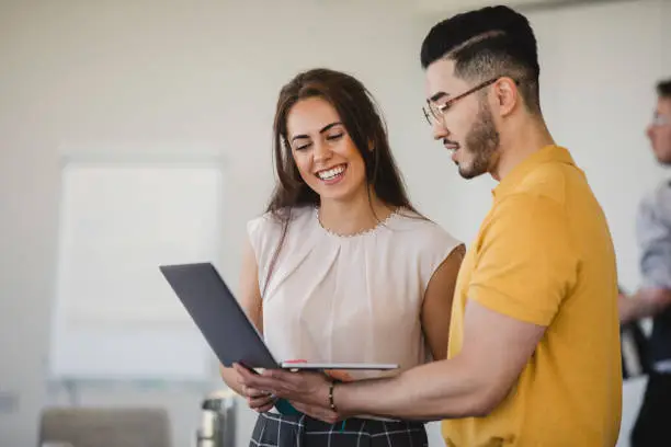 Photo of Hipster young man using laptop with cheerful female colleague