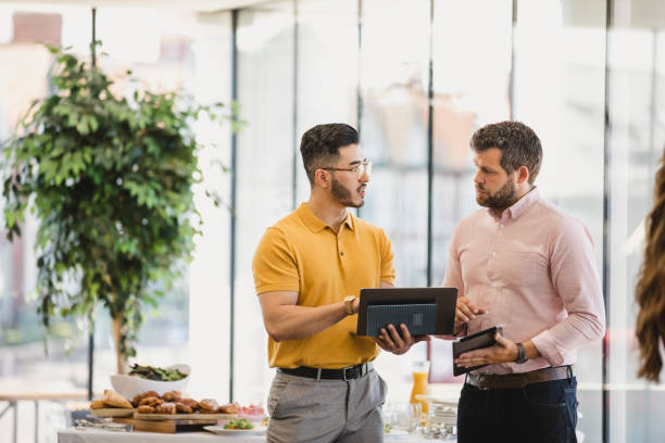 Young hipster man with laptop discussing with coworker