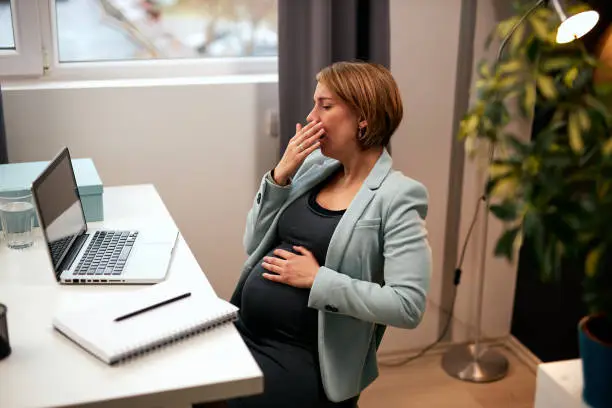 Tired caucasian pregnant employee yawning and sitting in her office.