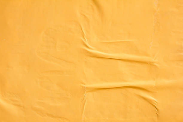 istock Orange crumpled poster glued on billboard. Orange gloss paper placard texture background. 1200931090
