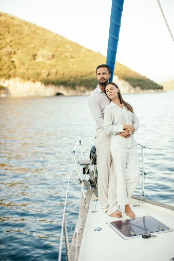 Beautiful young couple relaxing on sailboat's deck. They wear bright casual clothes and looks like they are in love