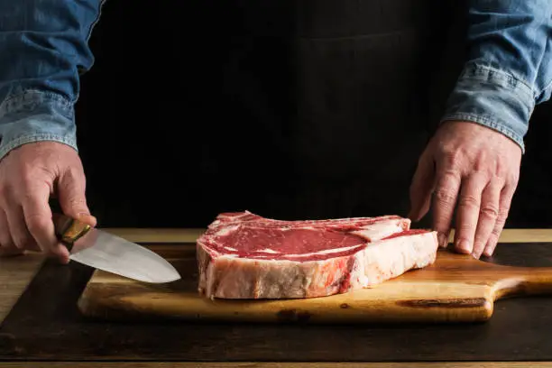 Man with a knife in his hand and a t-bone on a wooden kitchen board