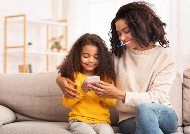 istock African Mother And Daughter Using Smartphone Sitting On Couch Indoor 1200932627