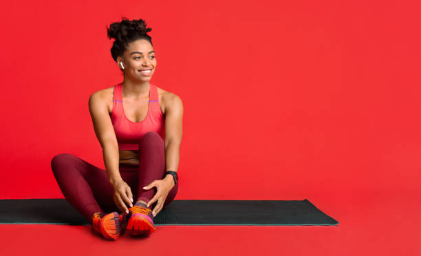 Happy fitness girl resting on yoga mat during training Happy black fitness girl resting on yoga mat during training, enjoying music with earbuds, copy space sportsman professional sport side view horizontal stock pictures, royalty-free photos & images