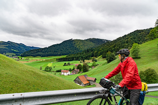 Bicycle traveler rests while climbing and looks at beautiful valley from where he had just climbed. Switzerland, Europe.