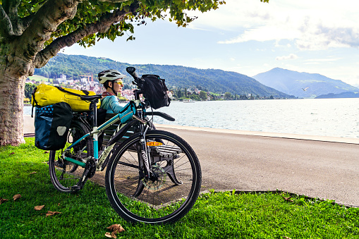 Woman bicycle traveler is resting on lake and looking into distance. Lake Zug (Zugersee), Switzerland, Europe.