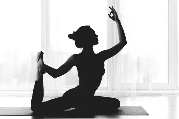 Silhouette of fit woman practicing yoga indoors over window Silhouette of fit woman practicing yoga indoors over panoramic window yoga studio photos stock pictures, royalty-free photos & images
