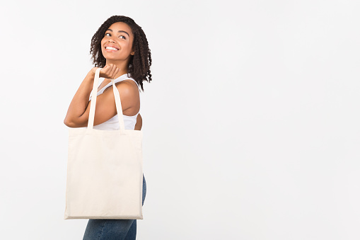 Ecology Concept. Black woman standing with white cotton bag looking at copy space over white background, mock up